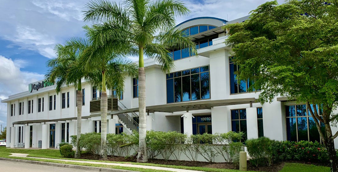 Exterior of 10070 Daniels Interstate Parkway property. White exterior with blue walls and palm trees