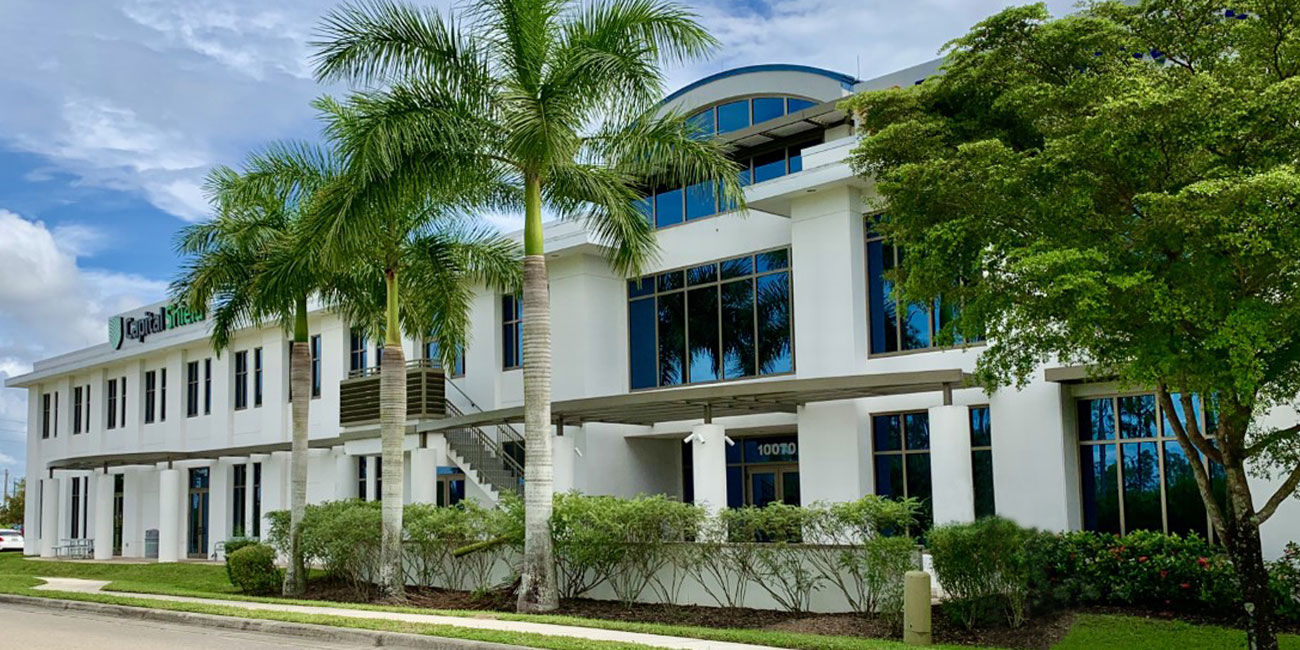 White stucco office building with dark blue windows and palm trees in Lee County Florida