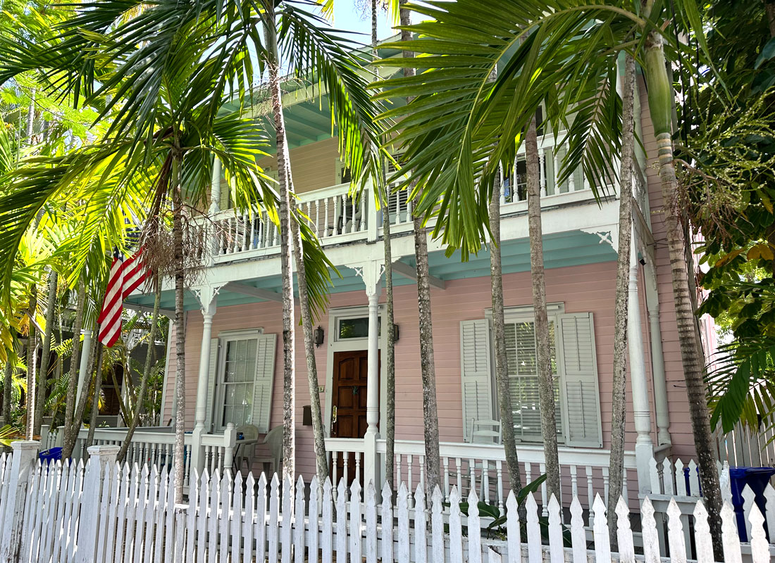 Home-Azure-Siesta-Key Light pink and teal blue historical home in the Florida Keys with white porch and picket fence.